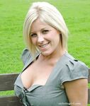 Clothed female with blonde hair shows off her red pumps in nylons on a bench