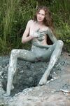 Naked teen girl with long legs covers herself in mud from head to toes