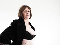 Old woman in leather boots and black 3 piece lingerie strips naked on sofa
