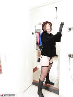 Old woman in leather boots and black 3 piece lingerie strips naked on sofa